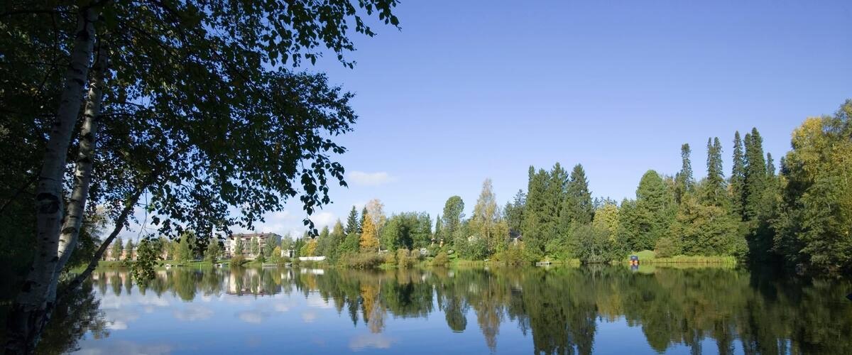 A calm lake reflecting trees and buildings.