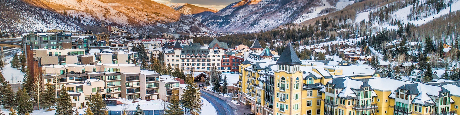 Un pueblo cubierto de nieve con montañas al fondo y un edificio amarillo destacado en el centro.