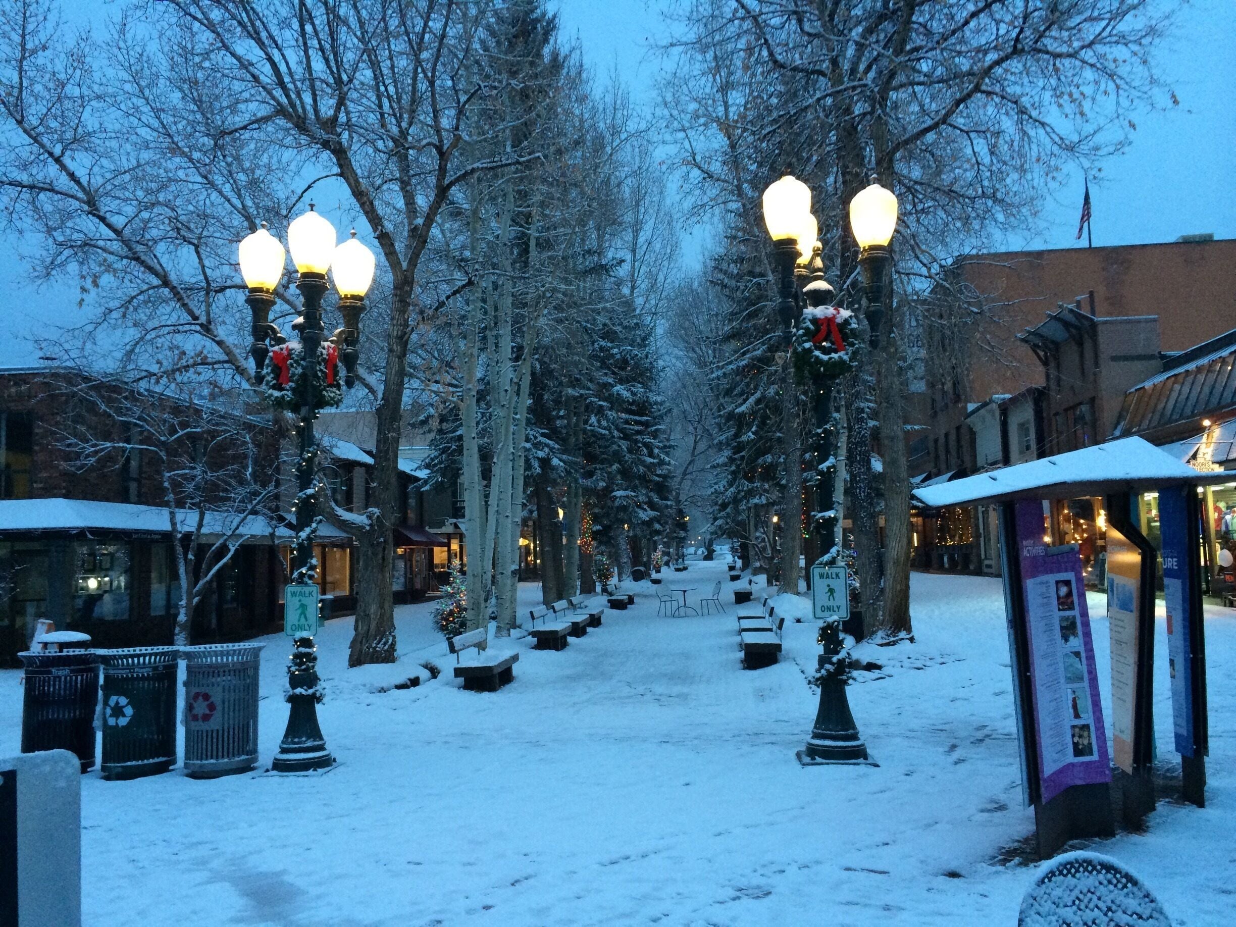 A snow-covered street with street lamps and benches.