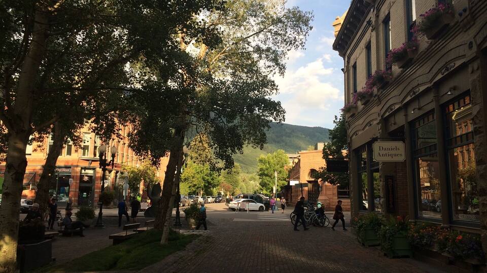 A tree-lined street with pedestrians, parked cars, and a building labeled "Daniels Antiques."
