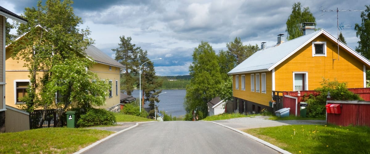A residential street with houses, a lake, and a cloudy sky.