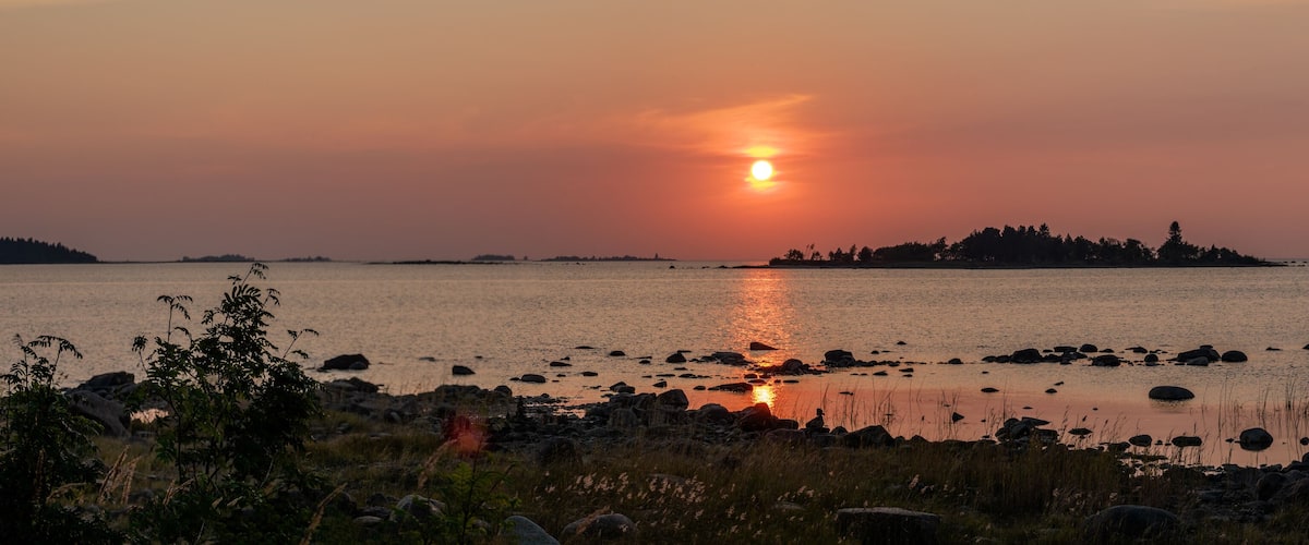 A sunset over a calm sea with a rocky shoreline and distant islands.