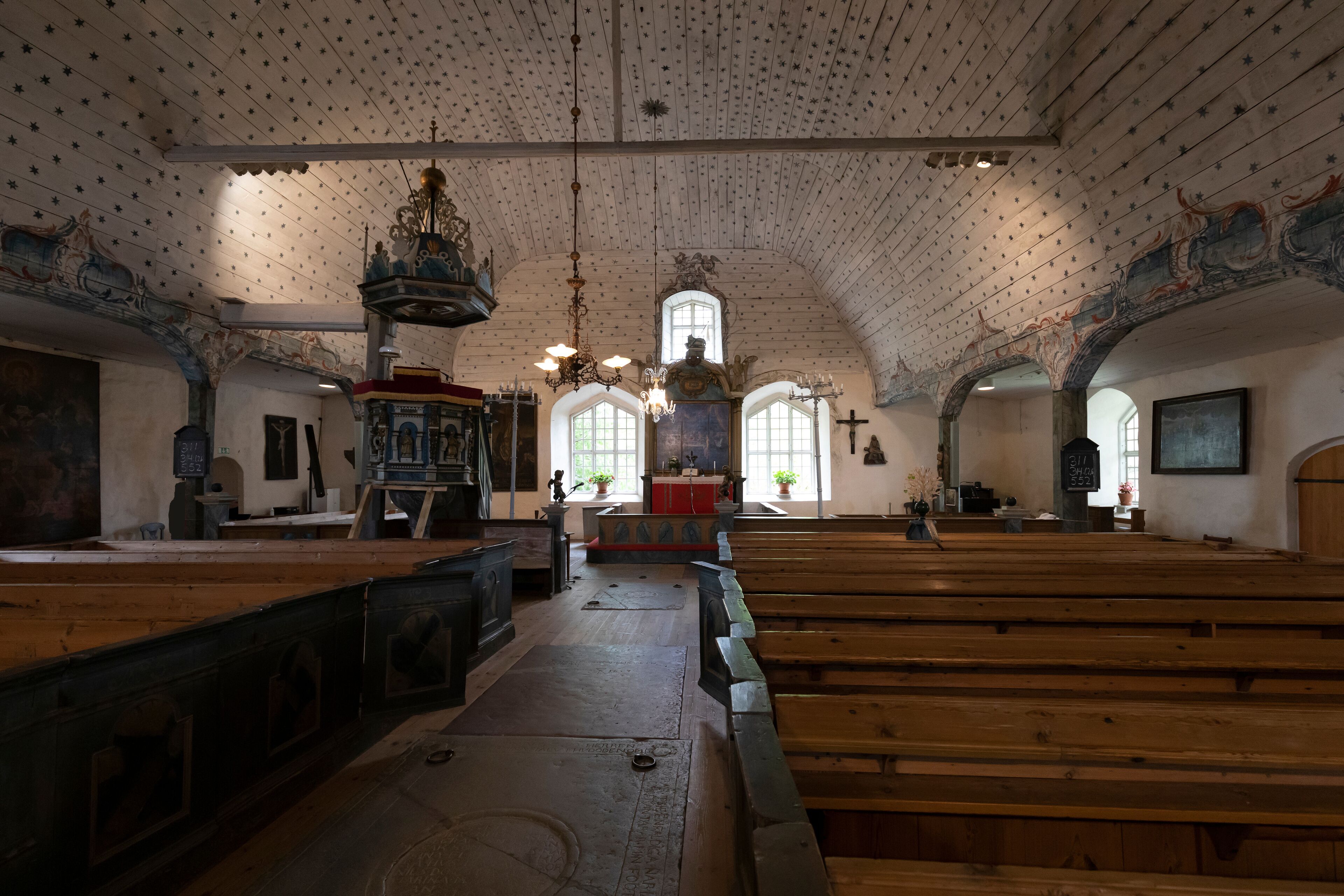 An interior with wooden pews, a high arched ceiling with star patterns, and a central altar with a chandelier.