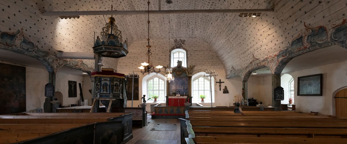 An interior with wooden pews, a high arched ceiling with star patterns, and a central altar with a chandelier.