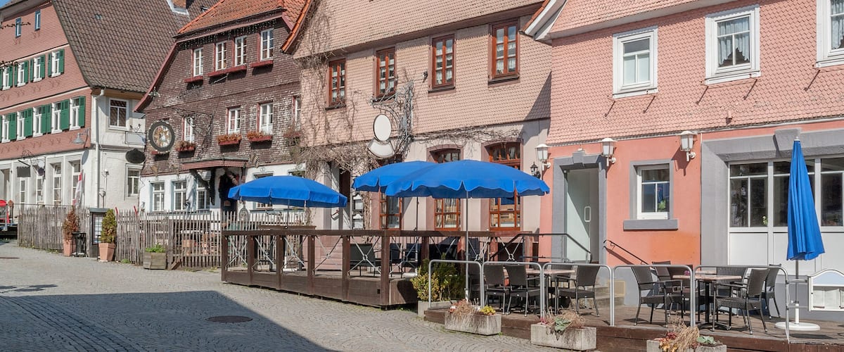 A cobblestone street lined with traditional European buildings, some with blue umbrellas.