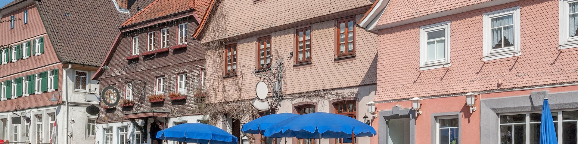 A cobblestone street lined with traditional European buildings, some with blue umbrellas.