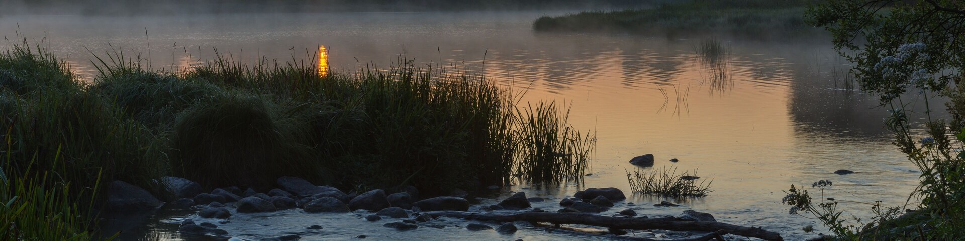 Un río al atardecer con rocas y vegetación.