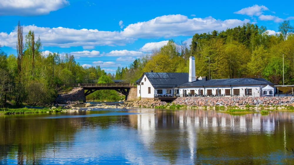 Un bâtiment situé au bord de la rivière, avec un pont, entouré d’arbres et sous un ciel dégagé.