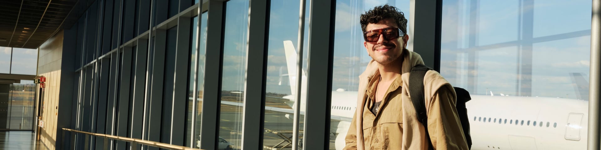 A person standing by a large window at an airport, holding a green object, with an airplane visible through the window.