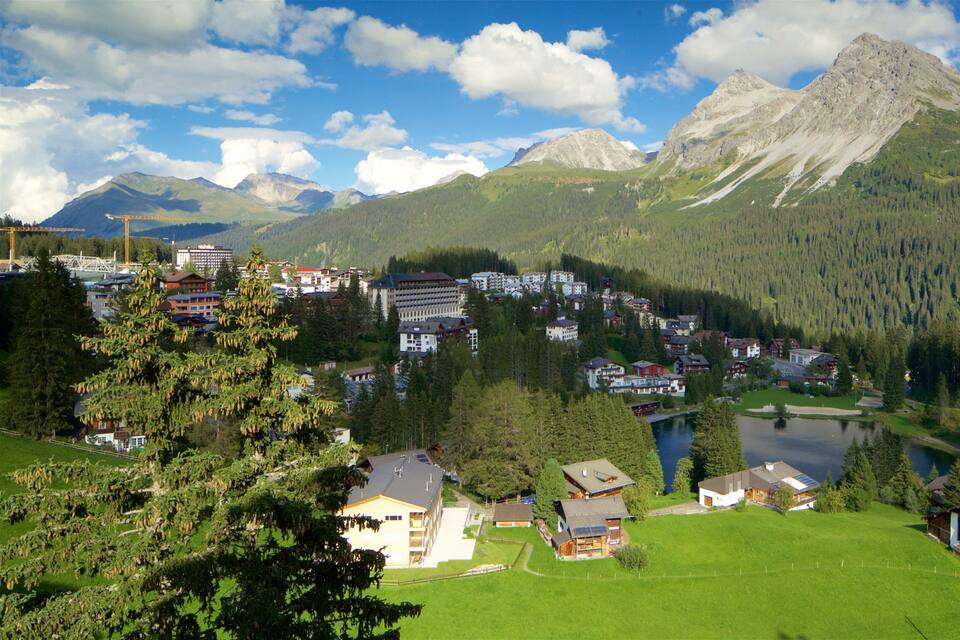 Un pueblo montañoso con un lago, rodeado de bosques densos y cumbres imponentes.