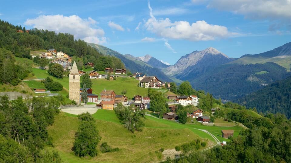 A picturesque village nestled in a valley with a prominent tower, surrounded by lush greenery and mountains.