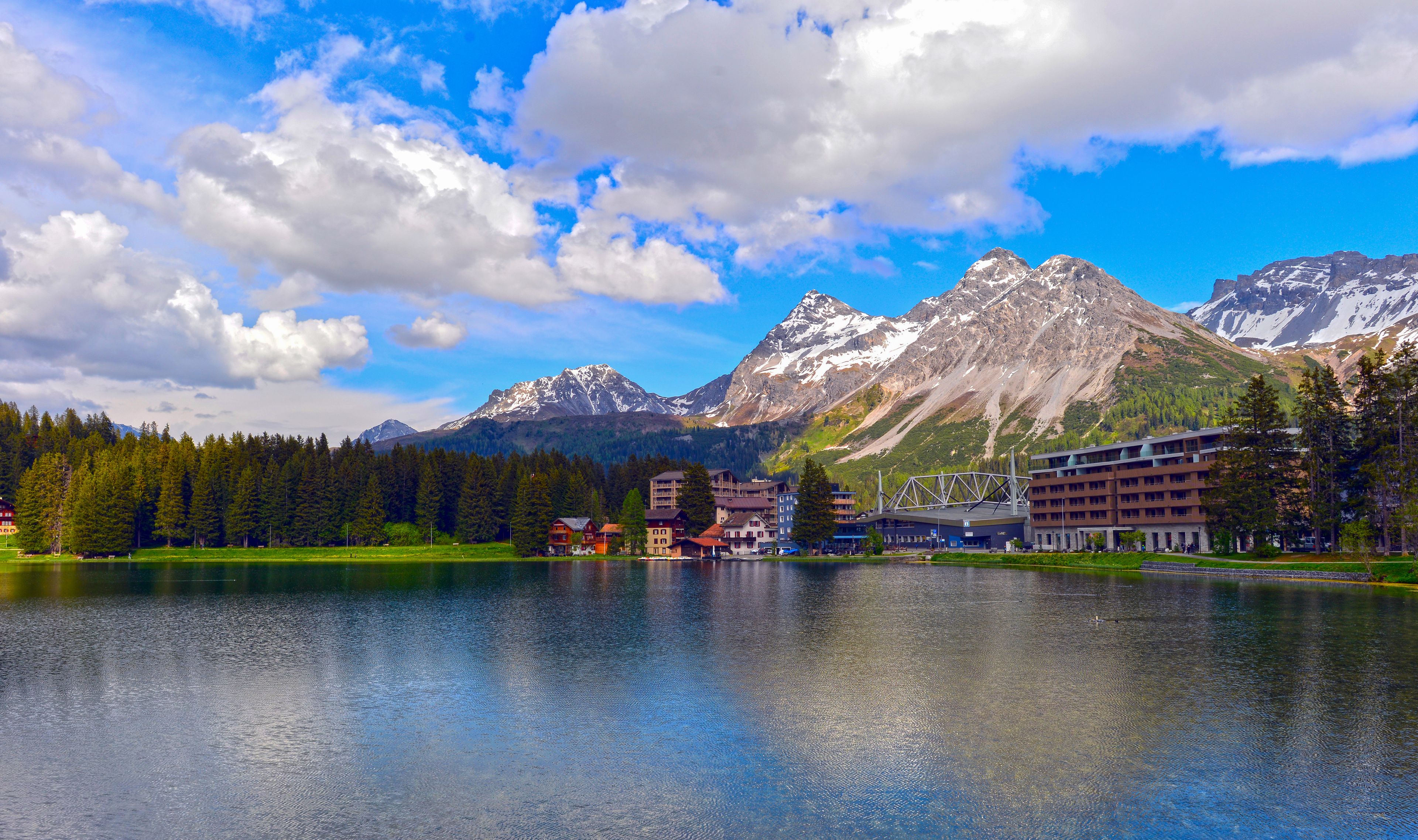 A lake with buildings and mountains in the background.