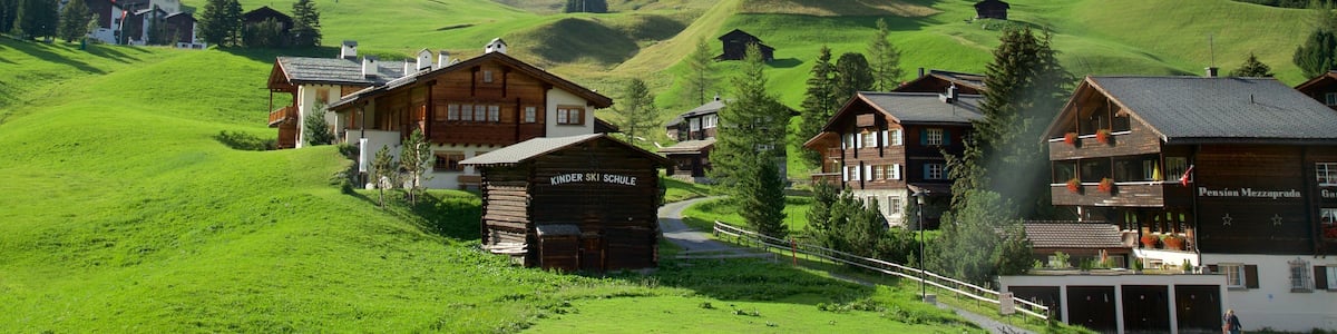 Ein Dorf mit Holzhäusern, einem Kindergarten und einem Berg im Hintergrund.
