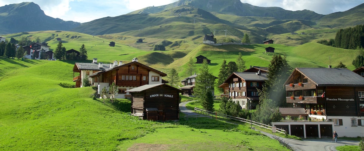 Un pueblo con casas de madera, un jardín infantil y una montaña al fondo.