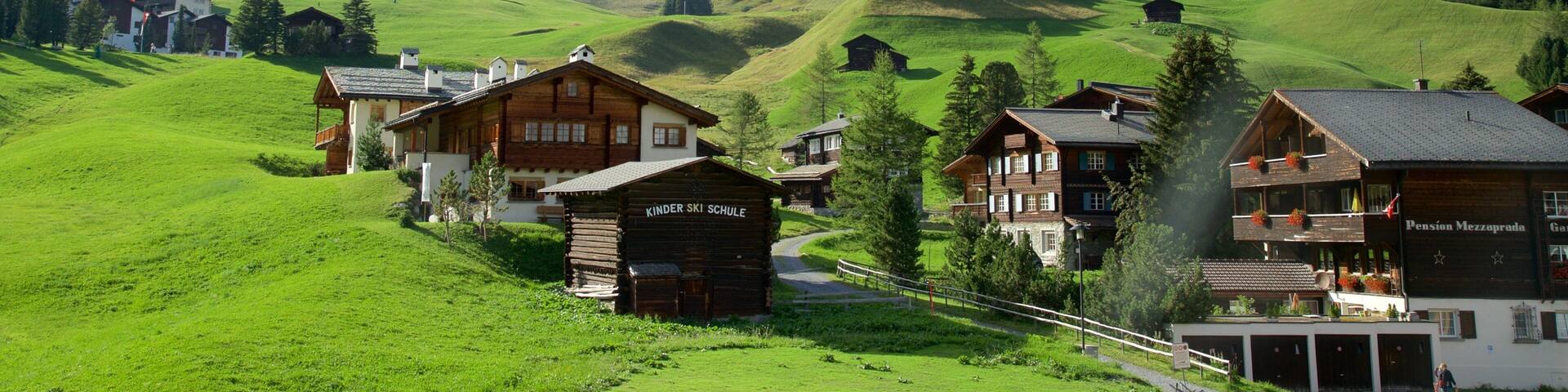 A village with wooden houses, a kindergarten, and a mountain in the background.