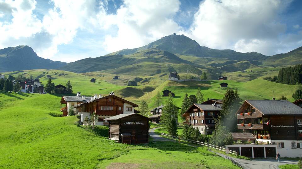 A village with wooden houses, a kindergarten, and a mountain in the background.