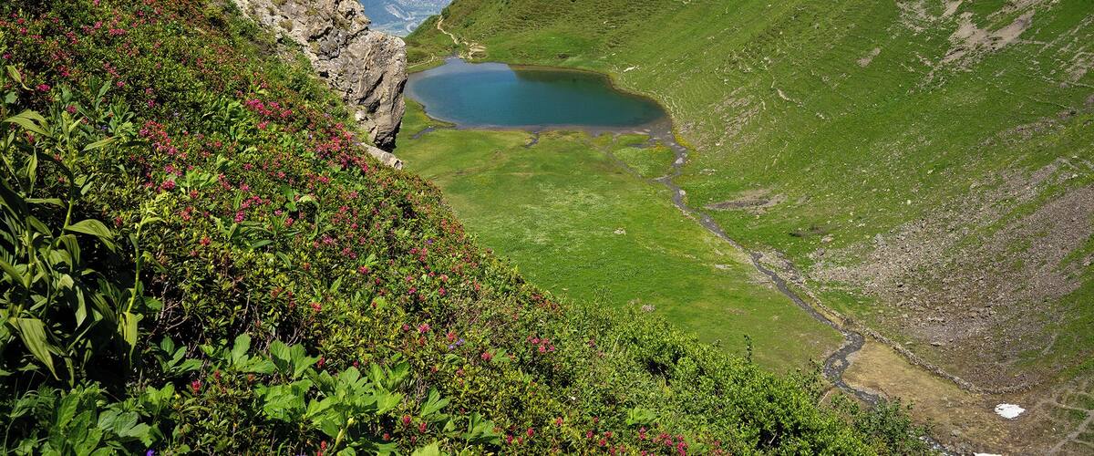 A mountain landscape with a lake, green slopes, and distant mountains.
