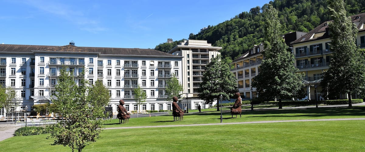 A large white building with multiple windows and balconies, surrounded by green grass and trees.