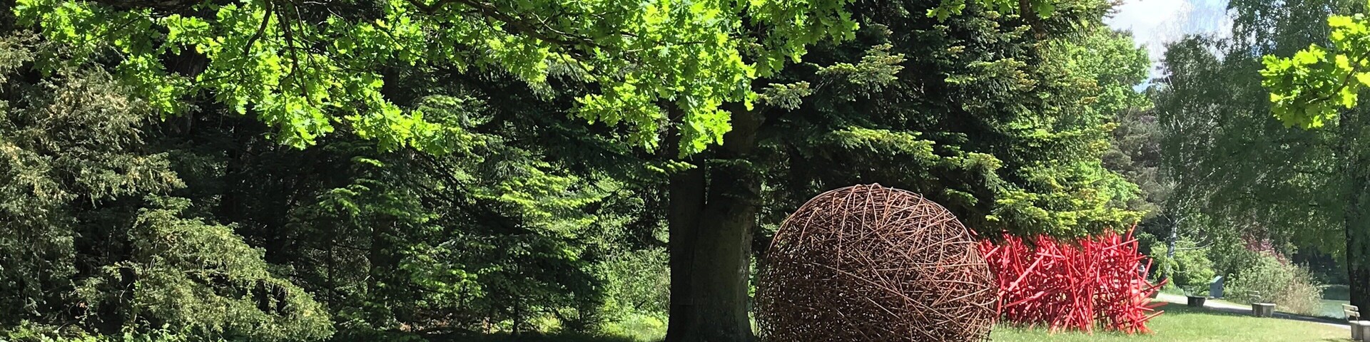 Un parque con un árbol grande, una escultura esférica y una estructura roja.