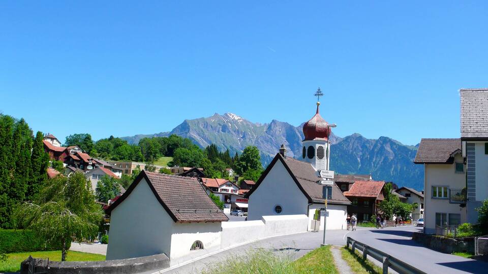 A village with white houses, a church with a red dome, and mountains in the background.