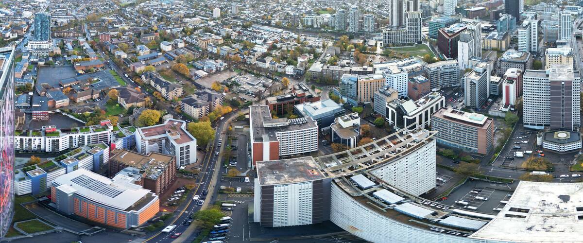 An aerial view of a city with modern architecture, including a distinctive curved building and a tall skyscraper.