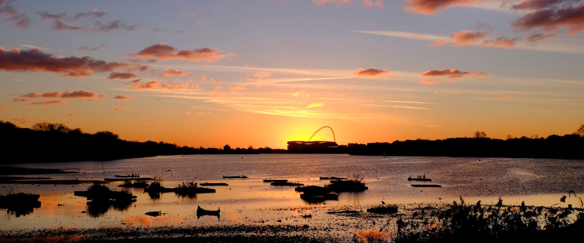 A sunset over a body of water with boats and a stadium in the background.