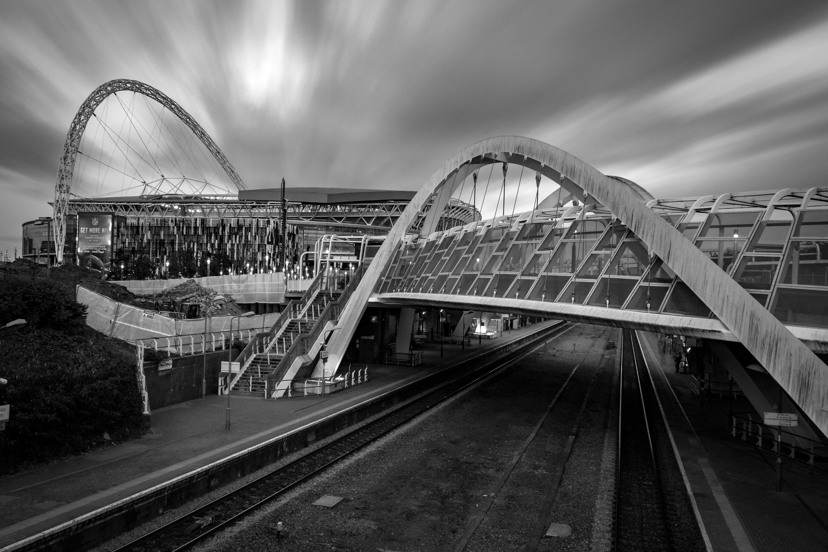 A modern train station with a distinctive arched bridge and a large circular structure in the background.