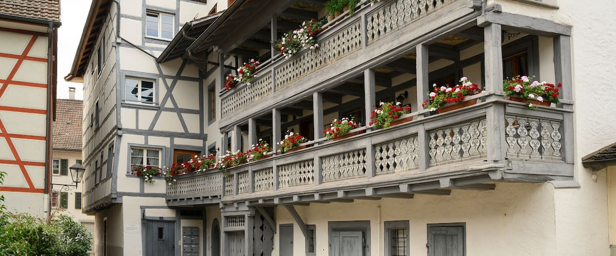 A traditional European building with multiple balconies adorned with flowers, wooden shutters, and a steeply pitched roof.