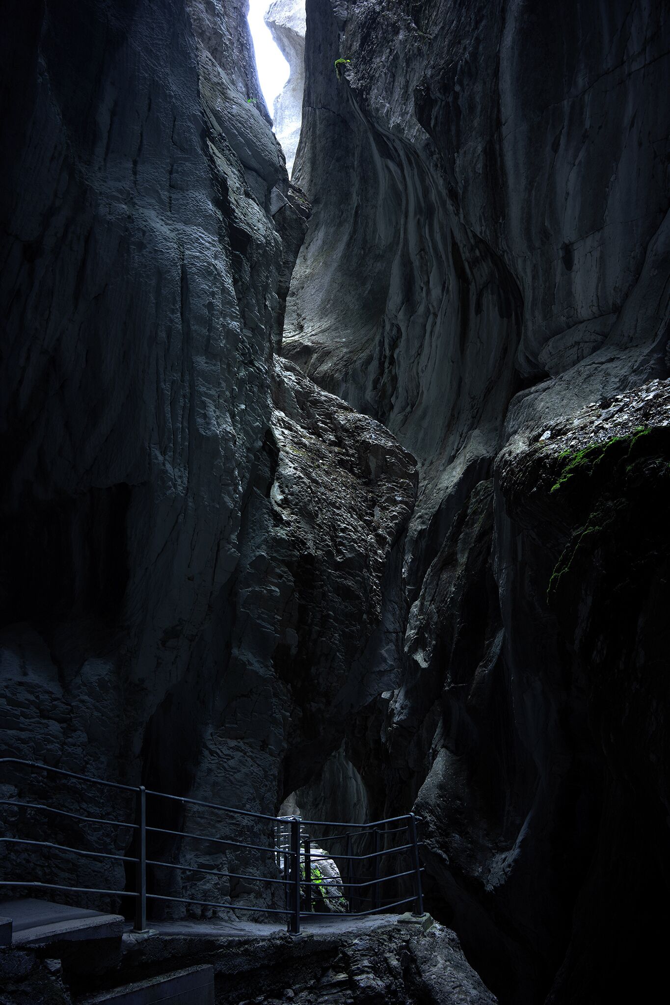 A narrow canyon with steep rock walls and a metal railing.