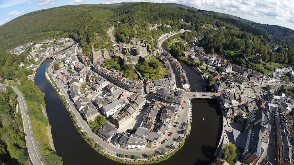 A river winding through a historic town with medieval architecture, surrounded by green hills.