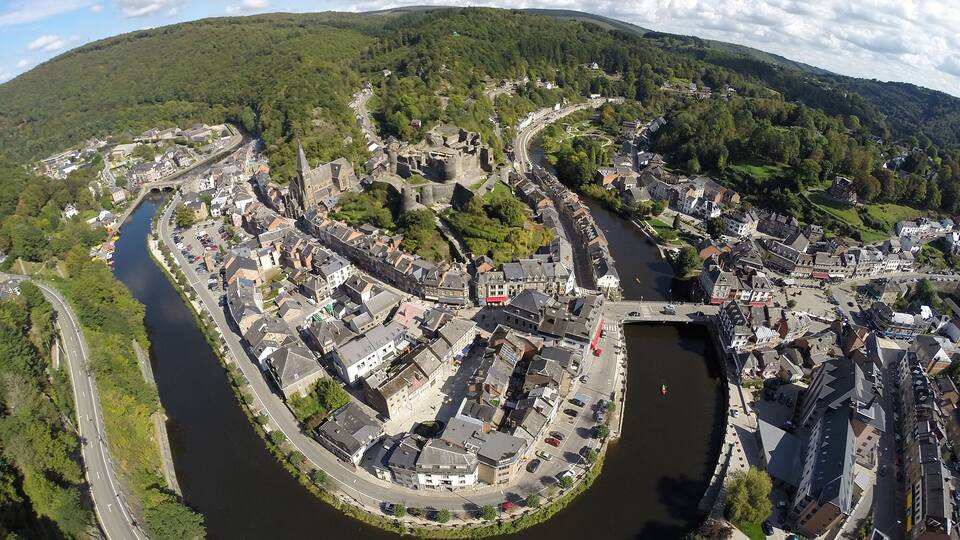A river winding through a historic town with medieval architecture, surrounded by green hills.