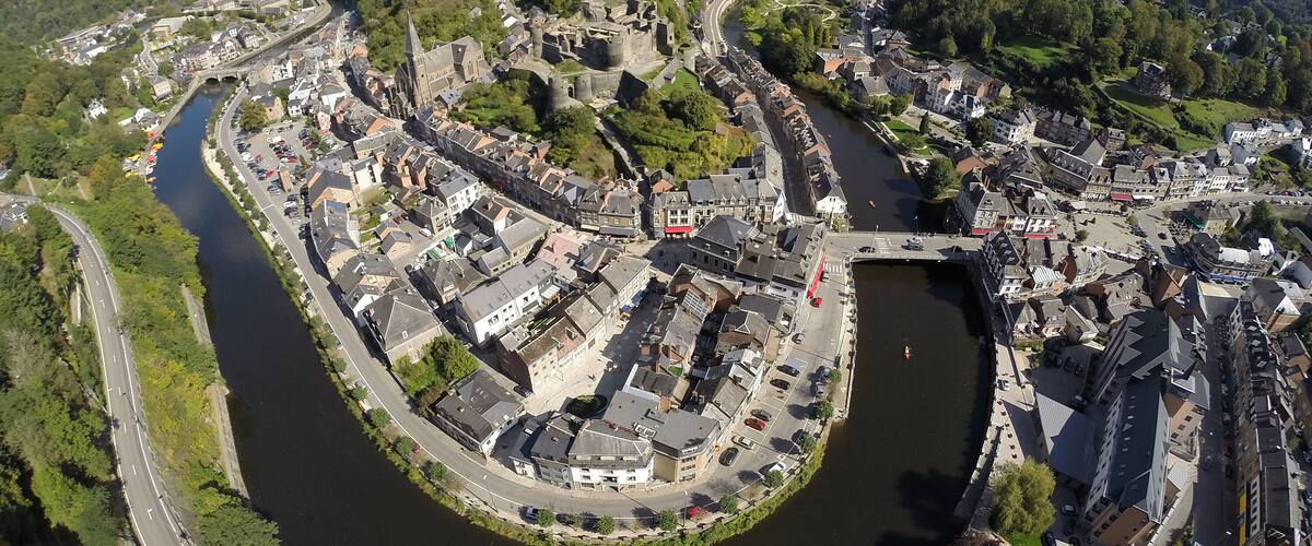 A river winding through a historic town with medieval architecture, surrounded by green hills.