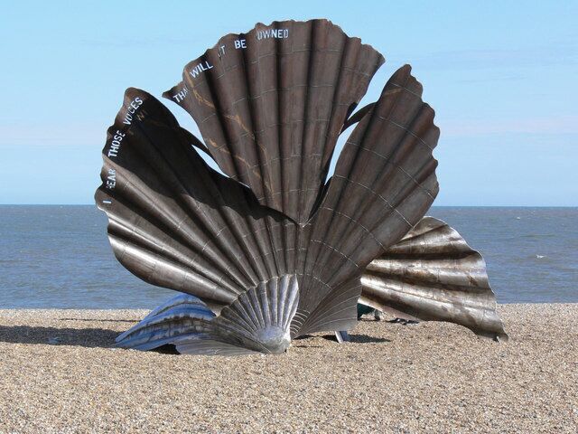 A large metallic shell sculpture on a pebble beach with the ocean in the background.