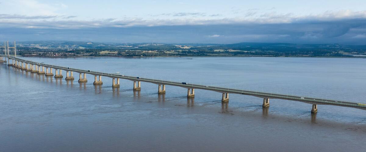 A long bridge over a calm river with a distant town and mountains.