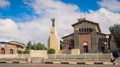 A church with a statue of a saint, a bell tower, and a mural on a building.