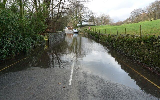 The B5285 flooded at Near Sawrey, Cumbria The yellow and white lines quickly disappeared from view under the water. I judged it be too deep to drive through. Fortunately the road was passable via a short cut behind the property to the left of this photograph. It took me five hours to drive from Near Sawrey to Kendal, normally a 14 mile drive.