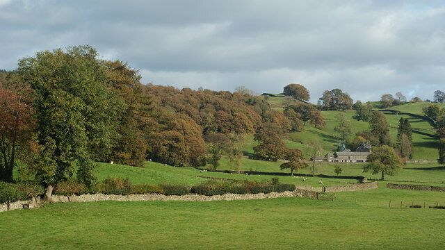 Rolling green hills, a stone wall, and a house in the distance.