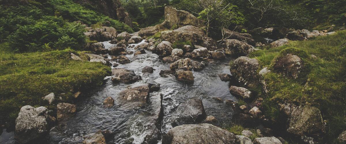 A rocky stream surrounded by lush green hills.