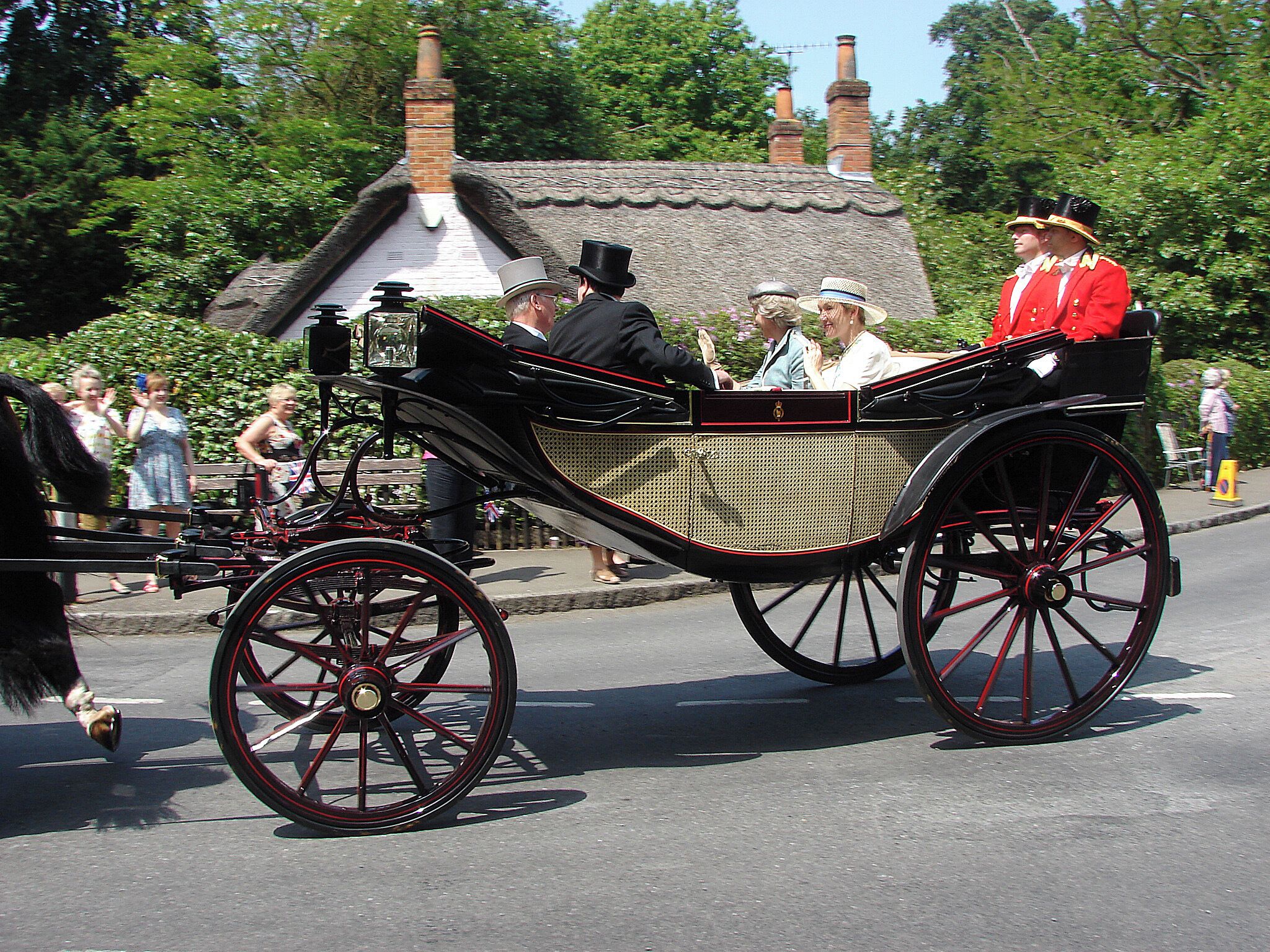 A horse-drawn carriage with passengers, a thatched-roof house, and lush greenery in the background.