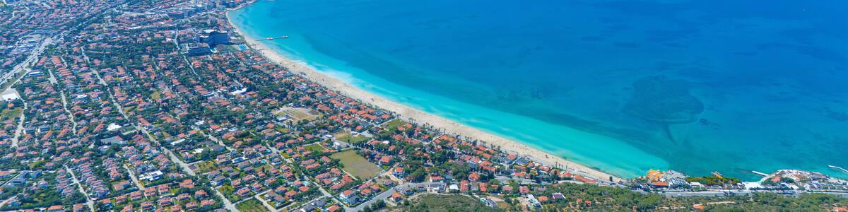An aerial view of a coastal city with a long beachfront, dense residential areas, and a clear blue sea.