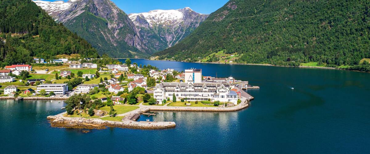 A coastal town with buildings, a harbor, and mountains with snow-capped peaks.