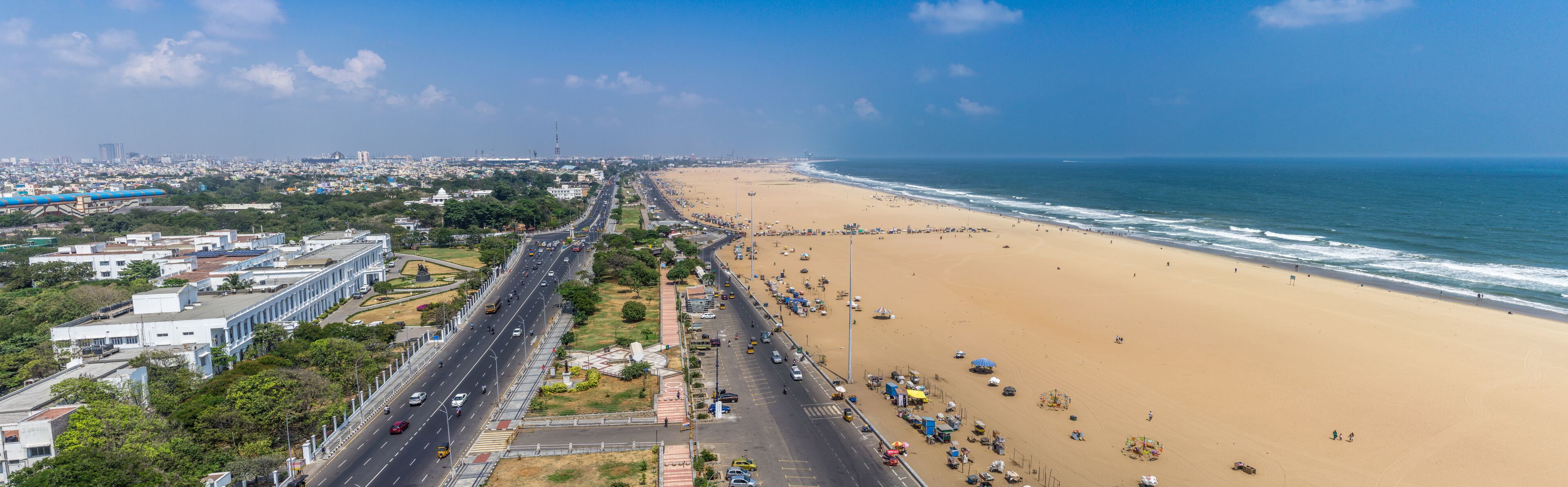A coastal city with a wide beach, a busy road, and urban buildings.