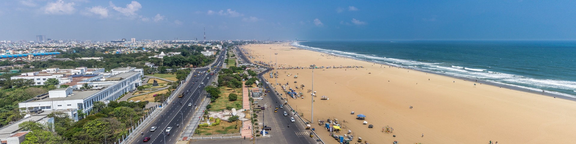 A coastal city with a wide beach, a busy road, and urban buildings.