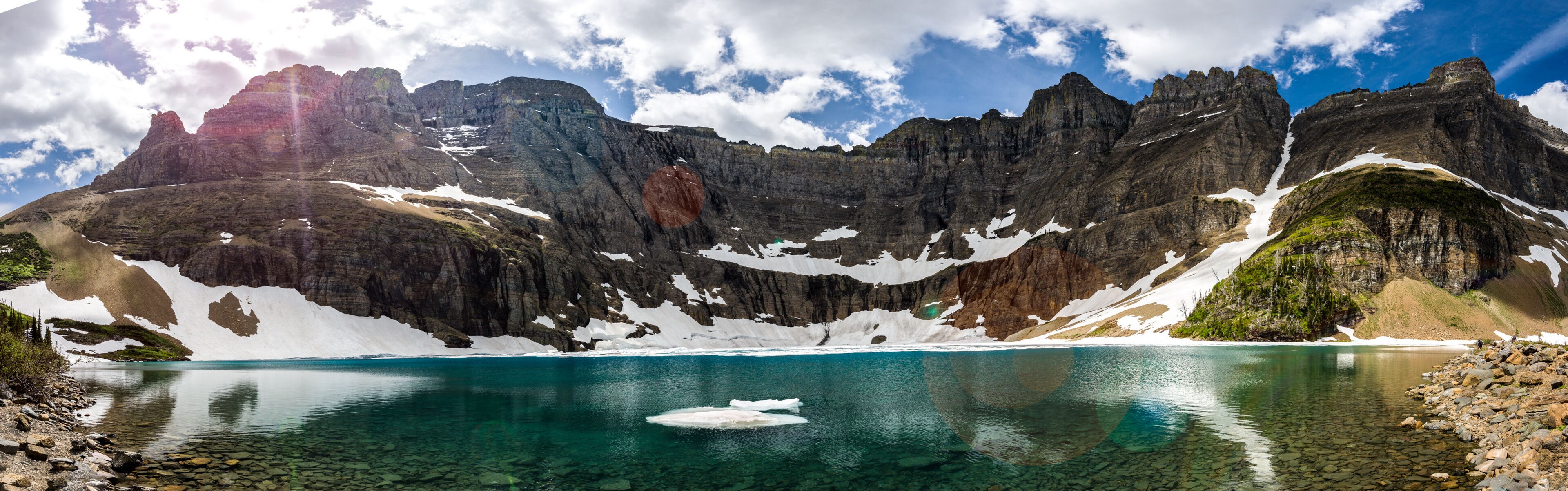 A mountain lake with clear water, surrounded by rocky cliffs and patches of snow.