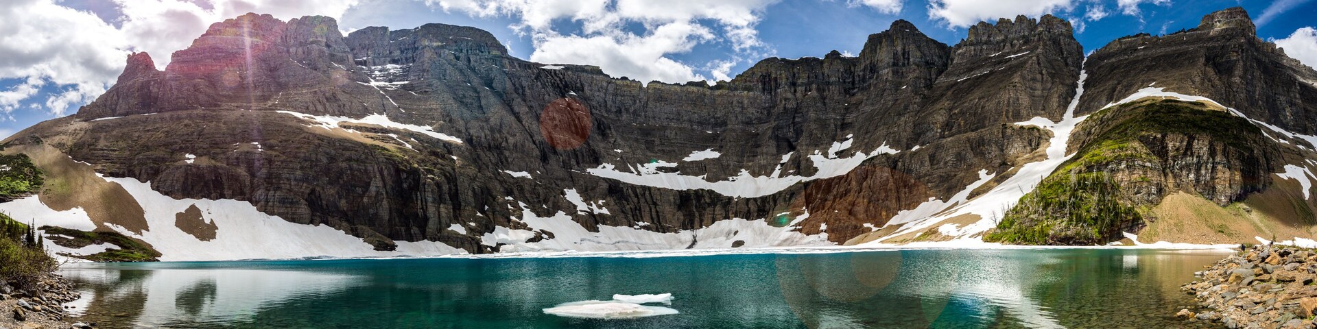 A mountain lake with clear water, surrounded by rocky cliffs and patches of snow.