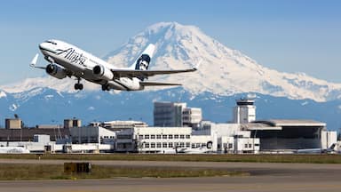 Um avião da Alaska Airlines decolando com uma montanha nevada ao fundo.