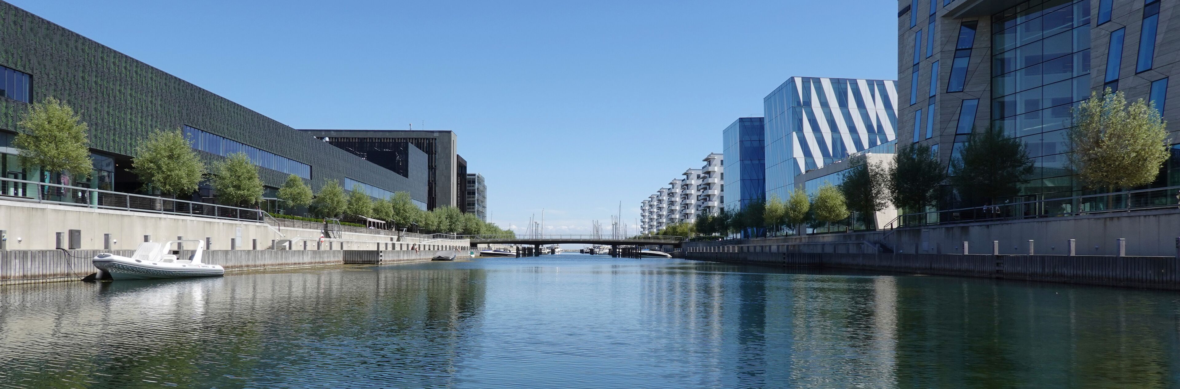 A canal with a boat, modern buildings, and a bridge.