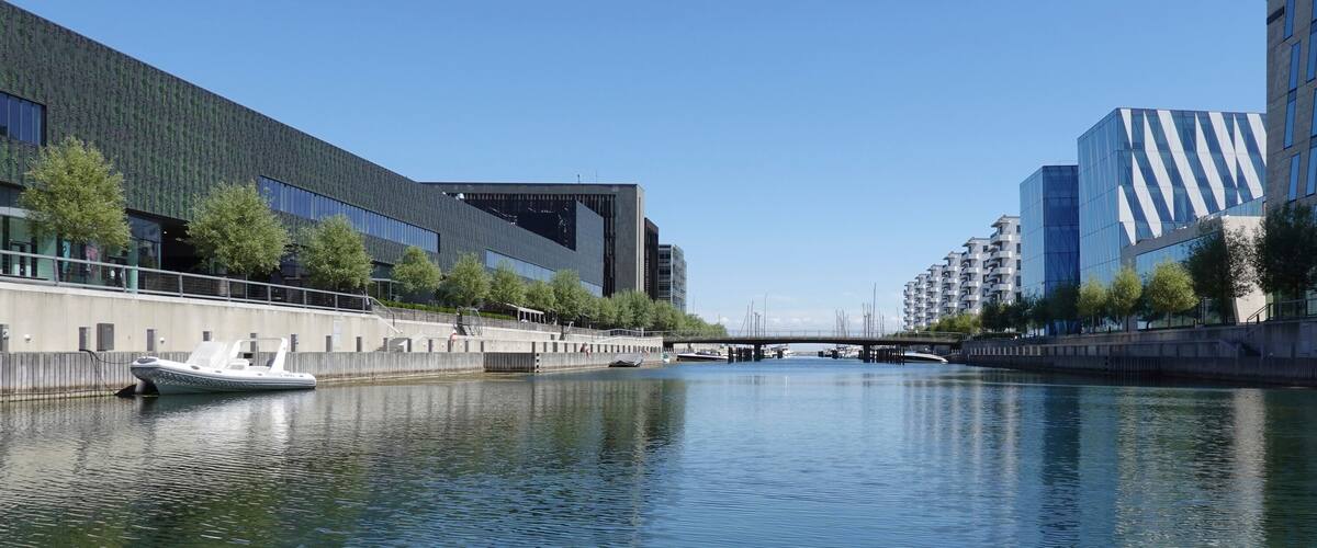 A canal with a boat, modern buildings, and a bridge.