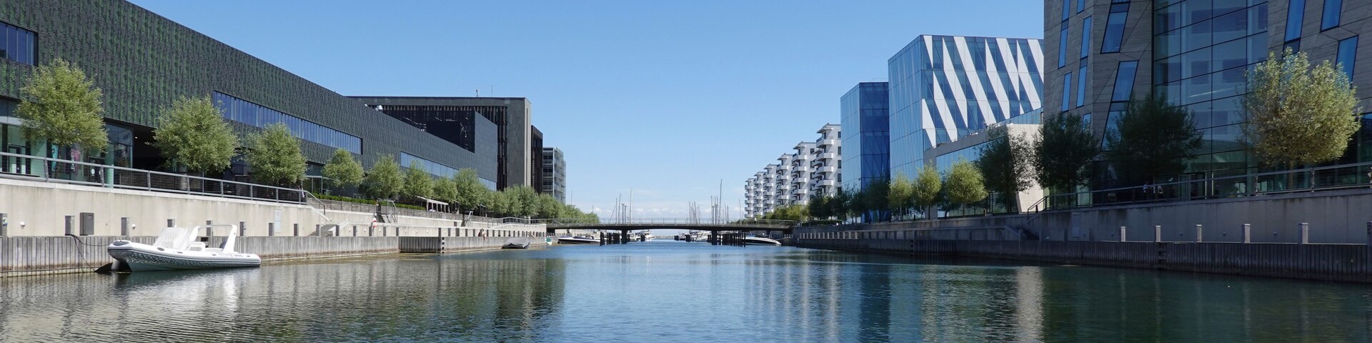 A canal with a boat, modern buildings, and a bridge.