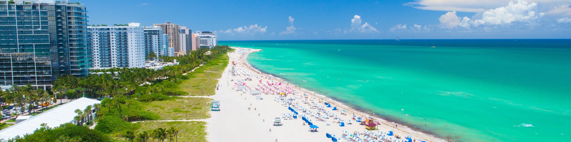 Uma praia com águas azul-turquesa, areia branca e uma fileira de edifícios altos ao fundo.